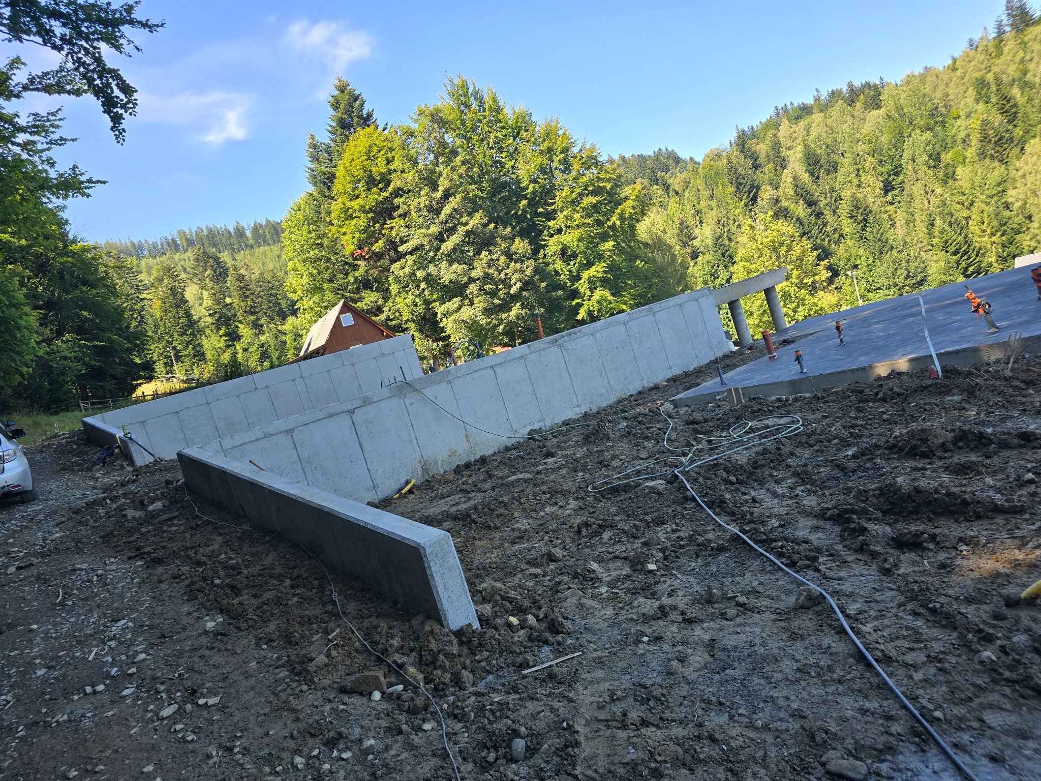 Wylane betonowe fundamenty z widoczną konstrukcją szalunkową na tle zalesionego terenu i błękitnego nieba.