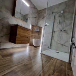 D&D USŁUGI REMONTOWO-BUDOWLANE PAWEŁ DUBIEL - Nowoczesna łazienka z drewnopodobnymi płytkami na podłodze, marmurowymi płytkami na ścianach, podwieszaną szafką z umywalką, toaletą w zabudowie i szklanym prysznicem typu walk-in.