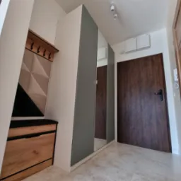 Nowoczesny przedpokój z szafą z lustrami, panelem wieszakowym z tapicerowanym siedziskiem i dwiema parami drzwi w odcieniach brązu.