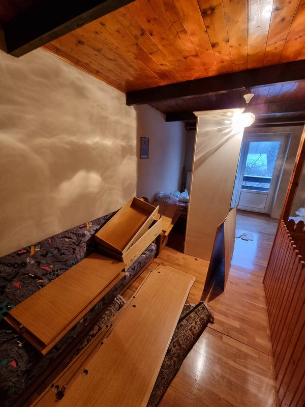 Demontaż mebli w trakcie remontu mieszkania: drewniane elementy szafy ułożone na sofie i podłodze, widoczne ślady po starych meblach na ścianie, sufit z drewnianą boazerią.