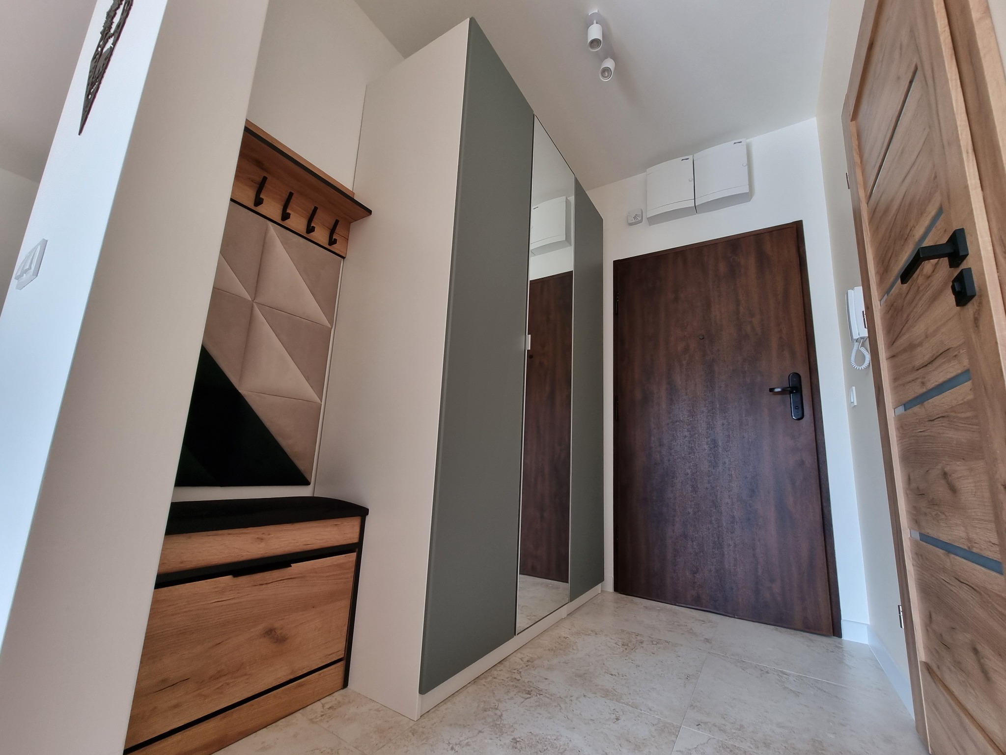 Nowoczesny przedpokój z szafą z lustrami, panelem wieszakowym z tapicerowanym siedziskiem i dwiema parami drzwi w odcieniach brązu.