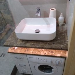 Grubud - Nowoczesna łazienka z prostokątną umywalką nablatową na blacie z brązowego lastryko, podświetlonym od dołu, oraz pralką Electrolux w zabudowie szafkowej z trzema szufladami.