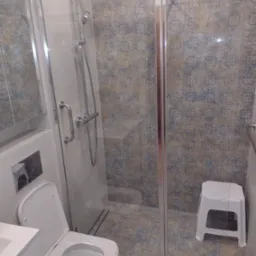 Wykończona łazienka z kabiną prysznicową ze szklanymi drzwiami, toaletą podwieszaną, wzorzystymi płytkami ściennymi i podłogowymi oraz małym białym stołkiem.