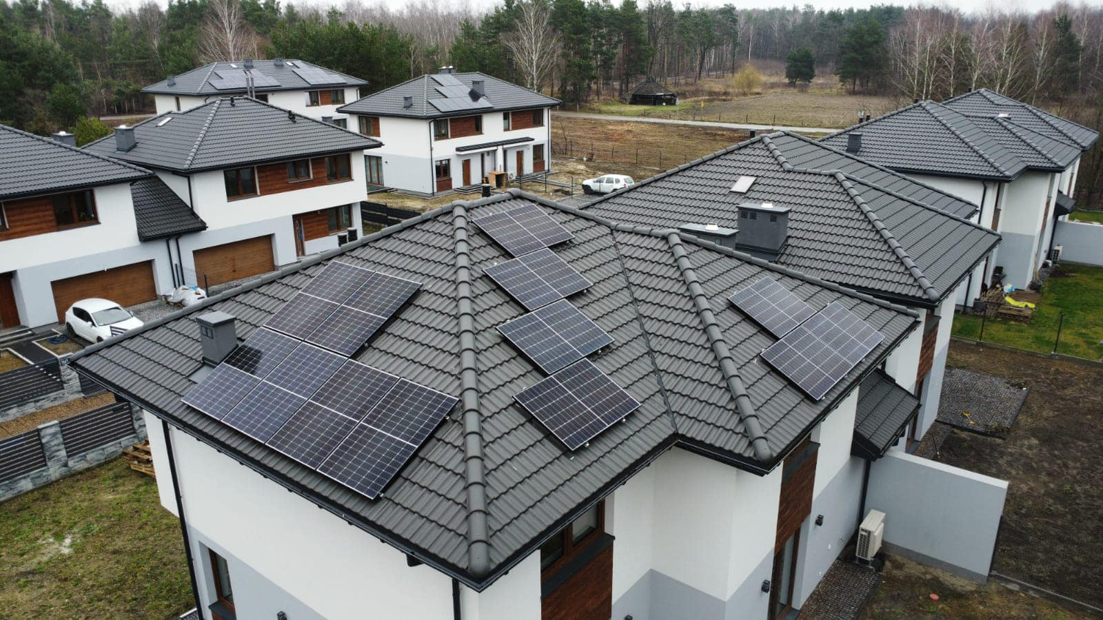 Panele słoneczne zamontowane na dachu domu z szarą dachówką, widok z góry na osiedle domów jednorodzinnych.