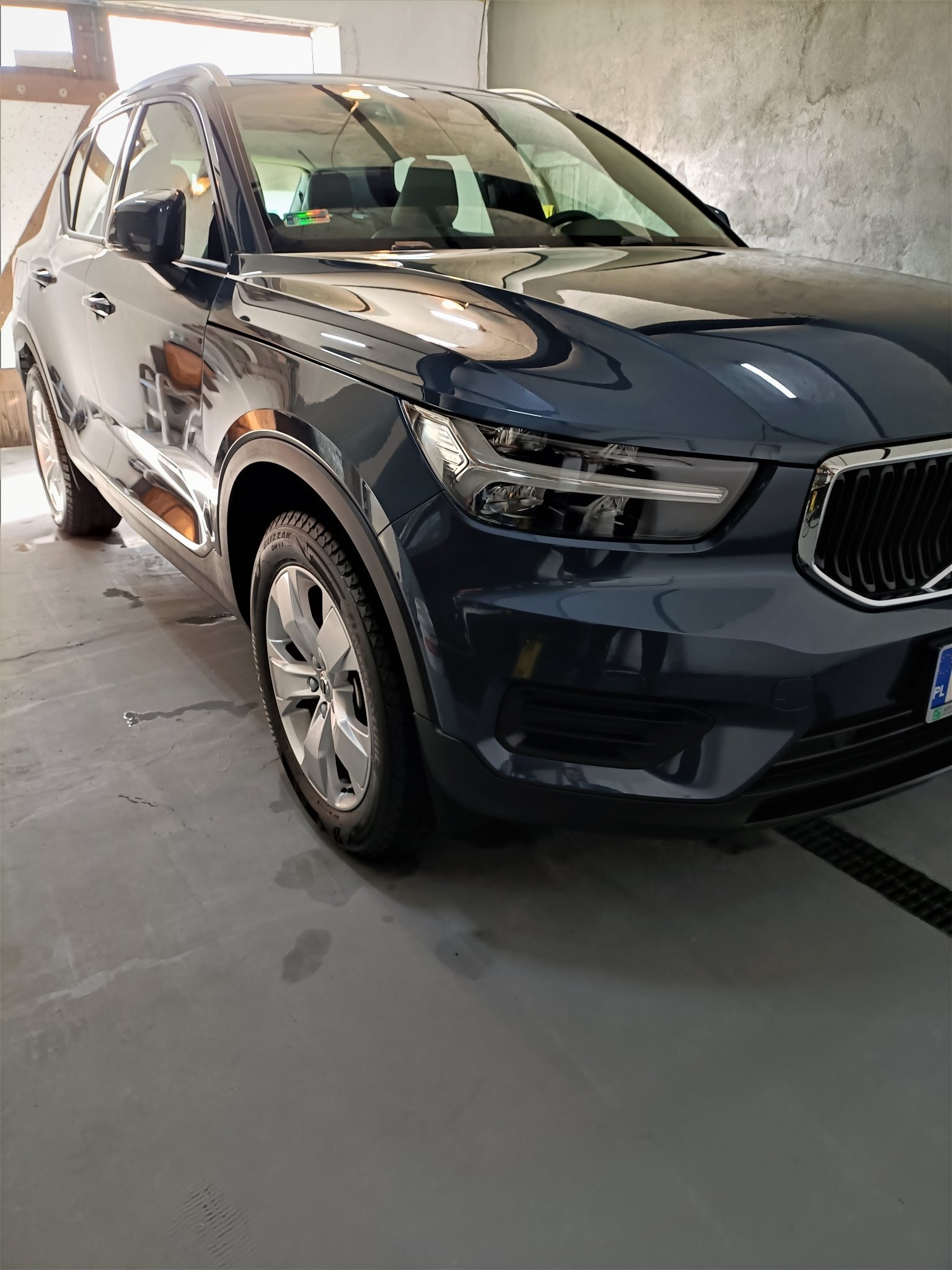 Ciemnoszary SUV Volvo XC40 po umyciu, widoczne krople wody na lakierze i oponach, na betonowej posadzce myjni.