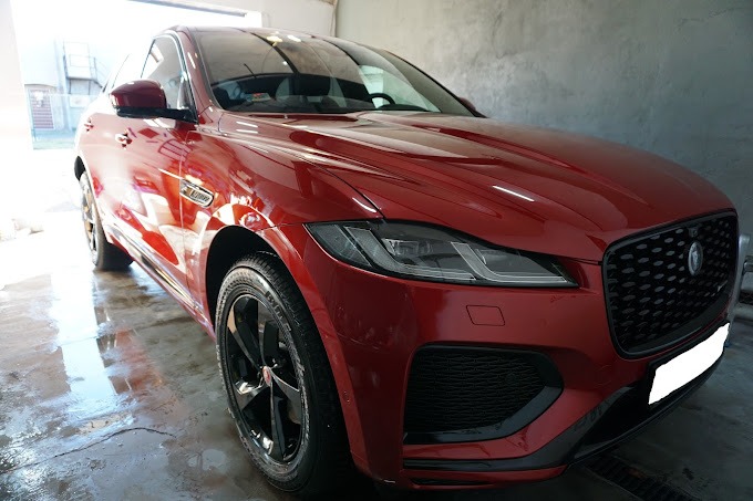 Błyszczący, bordowy Jaguar F-Pace po umyciu, z widocznymi kroplami wody na lakierze i mokrą posadzką myjni.