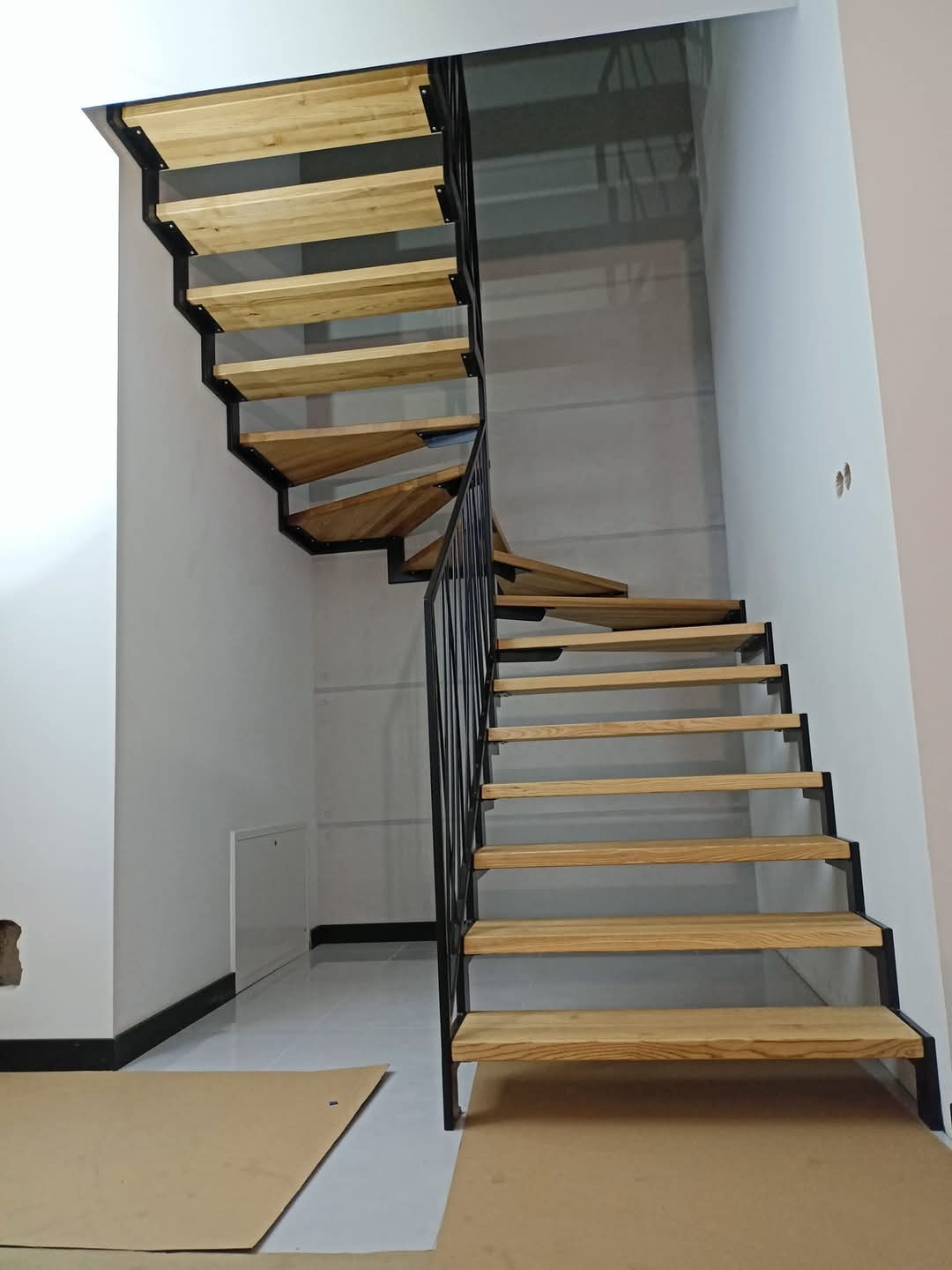 Spiralne schody z drewnianymi stopniami i czarną metalową konstrukcją w domu w Mieścisku, widoczne zabezpieczenia podłogi podczas montażu.