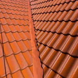 Czerwona dachówka ceramiczna po renowacji, widok z góry na błyszczącą powierzchnię i fragment systemu rynnowego w słoneczny dzień. Detal pokrycia dachowego.