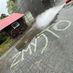 Michał Walczak M&W - Kostka brukowa czyszczona myjką ciśnieniową, na której widać wzór. W tle domek narzędziowy z czerwonym dachem i budynek gospodarczy. Ujęcie z góry, lekko pod kątem.
