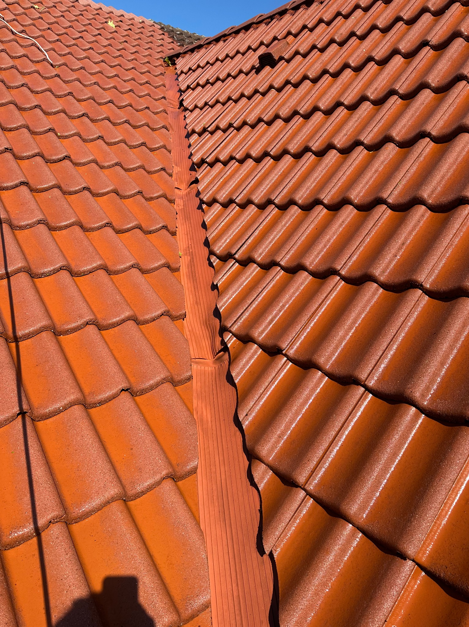 Czerwona dachówka ceramiczna po renowacji, widok z góry na błyszczącą powierzchnię i fragment systemu rynnowego w słoneczny dzień. Detal pokrycia dachowego.