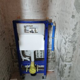 Stelaż podtynkowy Geberit Duofix zamontowany w surowej łazience, widoczne przyłącza wody. Ściany w stanie deweloperskim, przygotowane do dalszych prac wykończeniowych.