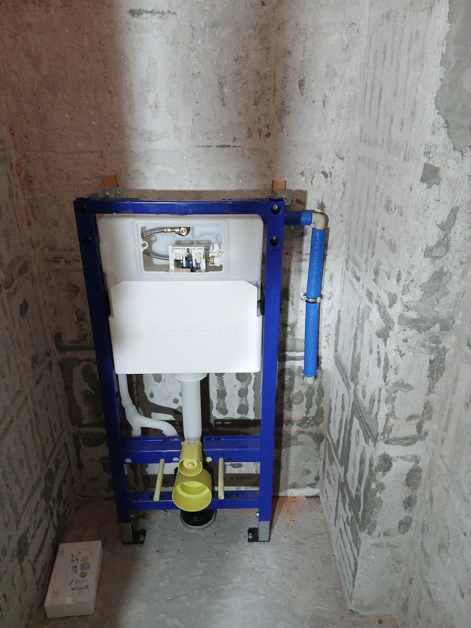 Stelaż podtynkowy Geberit Duofix zamontowany w surowej łazience, widoczne przyłącza wody. Ściany w stanie deweloperskim, przygotowane do dalszych prac wykończeniowych.