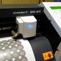 Alt-Press Krzysztof Żółtowski - Plotter tnący CAMM-1 GS-24 w trakcie wycinania okrągłych naklejek z napisem 'METAL PERFECT' i pięcioma gwiazdkami.