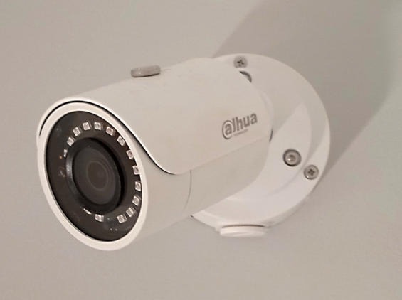 Biała kamera monitoringu Dahua zamontowana na jasnej ścianie, widoczne diody IR i śruby mocujące.