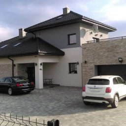 U. Kozioł, G. Kozioł sp. jw. - Nowoczesny dom jednorodzinny z czarną bramą garażową, oknami i dachem, na podjeździe stoją dwa samochody, widoczny zza ogrodzenia.