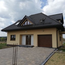 U. Kozioł, G. Kozioł sp. jw. - Nowoczesny dom jednorodzinny z brązową bramą garażową, jasną elewacją i brukowanym podjazdem w trakcie wykańczania.