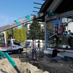 U. Kozioł, G. Kozioł sp. jw. - Montaż okna z użyciem podnośnika próżniowego, pracownicy poziomują okno, widoczny samochód dostawczy z oknami w tle.