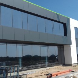 U. Kozioł, G. Kozioł sp. jw. - Nowoczesny budynek biurowy z fasadą z paneli aluminiowych i dużymi oknami, widoczne elementy montażowe i rury na ziemi.