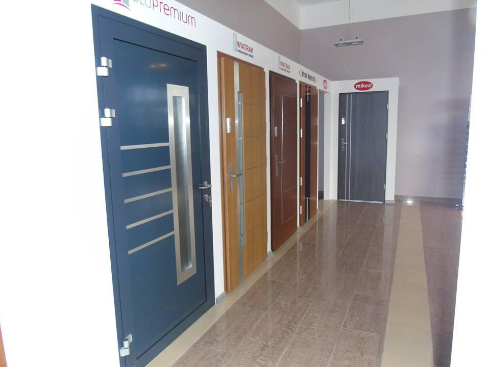 Ekspozycja różnych modeli drzwi zewnętrznych w salonie, widoczne drzwi antywłamaniowe z przeszkleniem i metalowymi listwami oraz inne modele z różnymi wykończeniami.