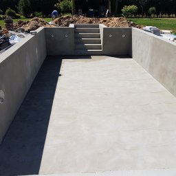 Majsterhome - Surowa betonowa konstrukcja basenu w ziemi z wbudowanymi schodami, przygotowana do dalszych prac wykończeniowych, z widocznymi instalacjami i otoczeniem budowy.