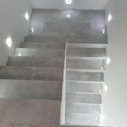 Majsterhome - Wykończone schody z szarych płytek, oświetlone punktowymi lampami w ścianach i suficie. Minimalistyczny design, widok z góry.