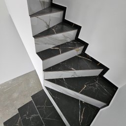 Majsterhome - Wykończone schody z czarno-białych płyt marmurowych, widok z góry, z fragmentem surowej betonowej podłogi. Minimalistyczne połączenie bieli ścian i wzoru kamienia.