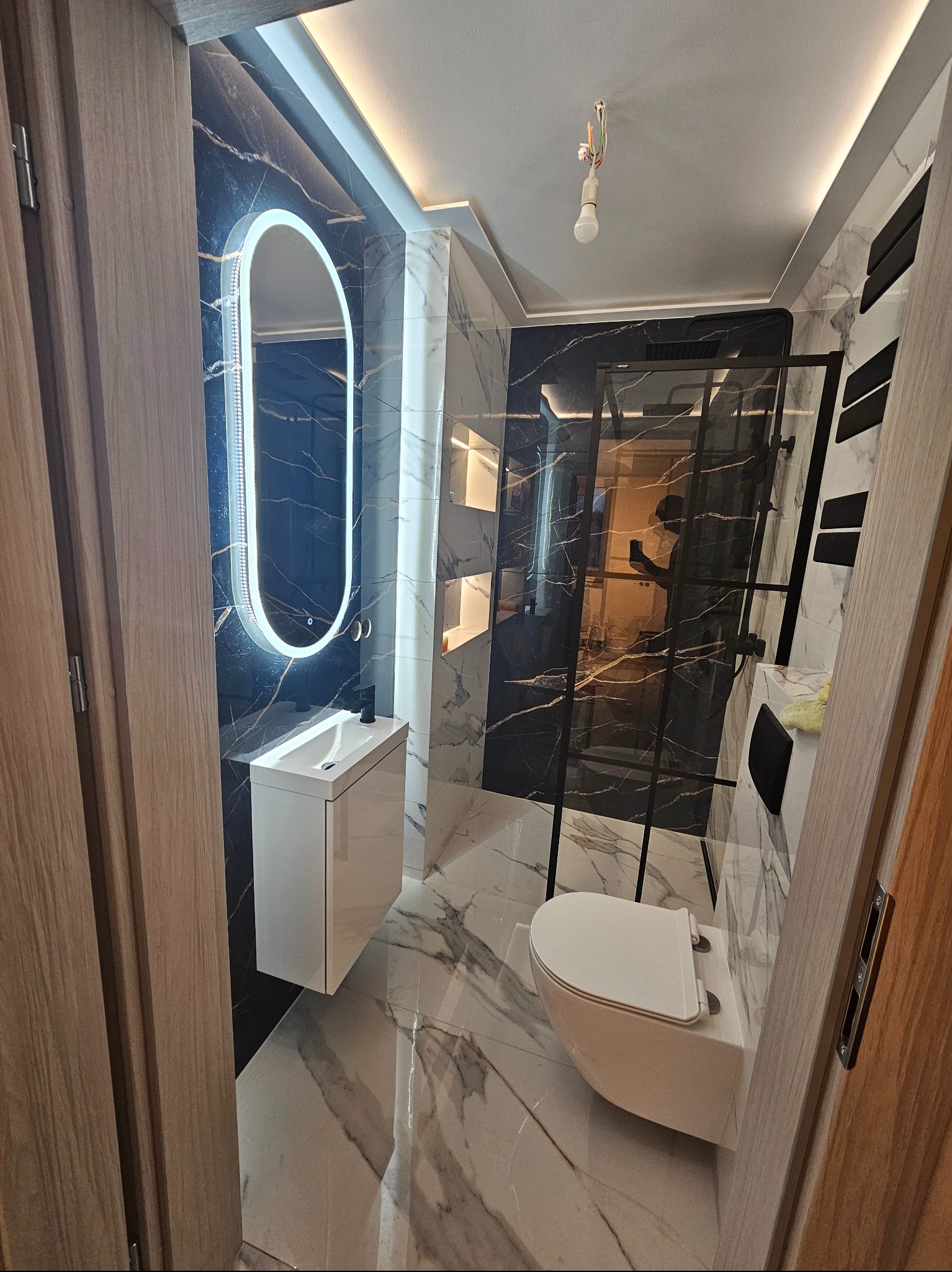 Wykończona łazienka z czarnymi i białymi marmurowymi płytkami, podświetlanym lustrem, kabiną prysznicową i podwieszaną toaletą. Nowoczesny design.