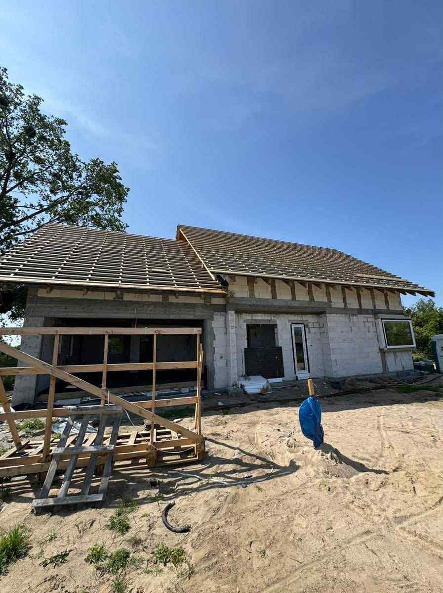 Budowa domu jednorodzinnego w stanie surowym otwartym: ściany z betonu komórkowego, więźba dachowa. Na pierwszym planie drewniany element konstrukcyjny.