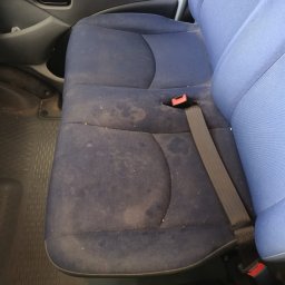FRESHAUTO KAROL BOBRO - Brudne, niebieskie siedzenie samochodowe z plamami i zapiętym pasem bezpieczeństwa, widoczne elementy wnętrza pojazdu.