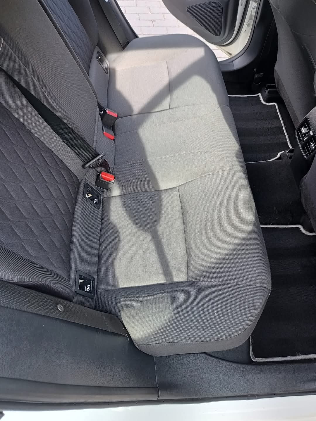 Wnętrze samochodu: tylna kanapa po czyszczeniu, widoczne pasy bezpieczeństwa i czarna wykładzina z białym obszyciem.