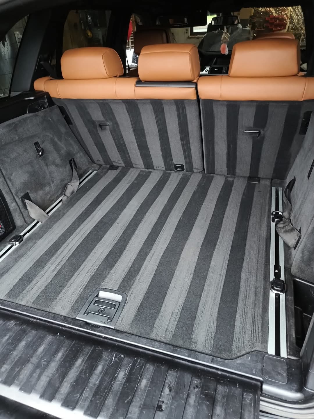 Wnętrze bagażnika samochodu SUV z wypraną, czystą tapicerką w szaro-czarne pasy, widoczne brązowe zagłówki tylnych siedzeń.