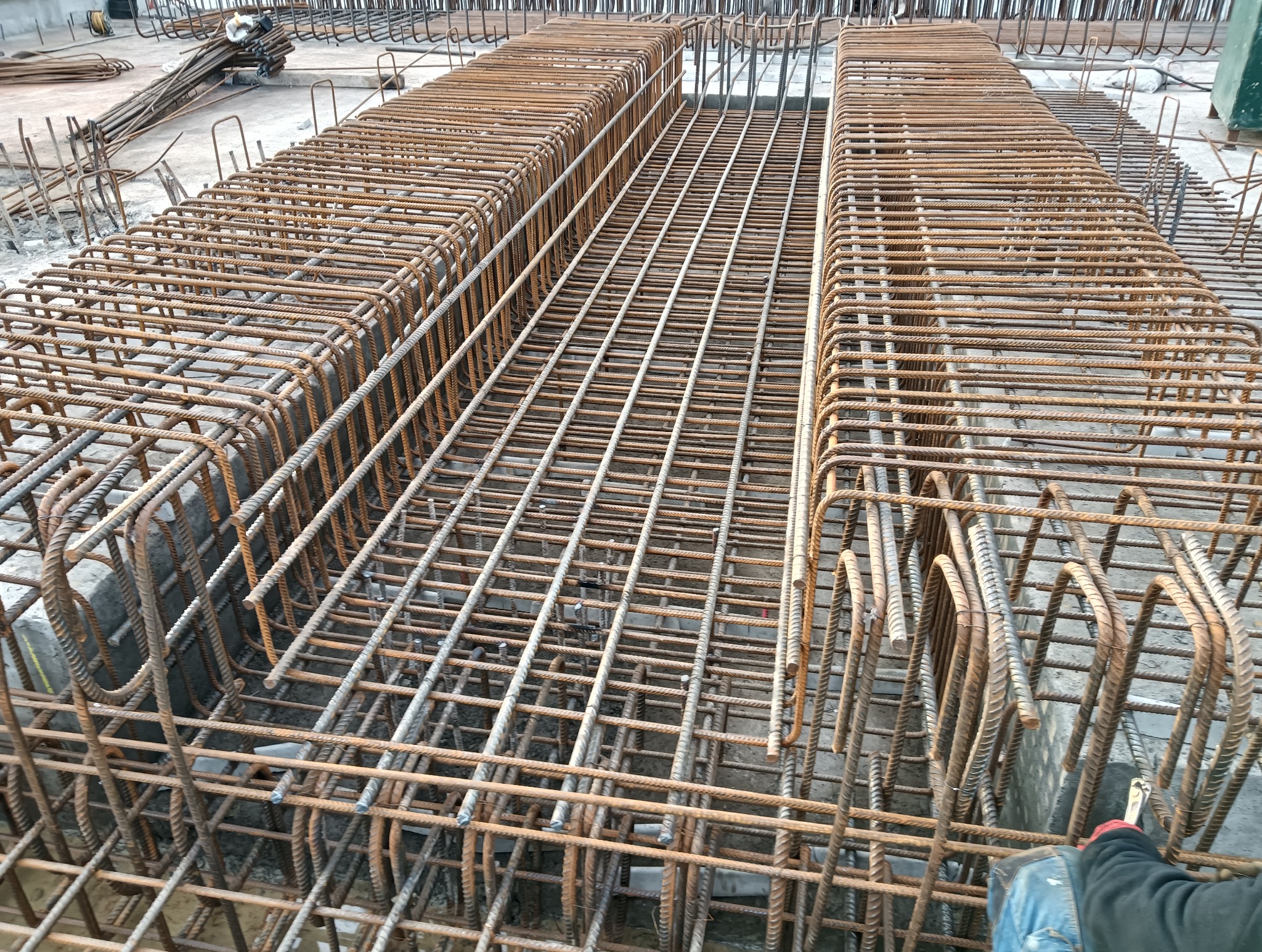 Siatka zbrojeniowa ułożona w szalunku, widoczne liczne pręty zbrojeniowe uformowane w regularną strukturę, przygotowane do zalania betonem.