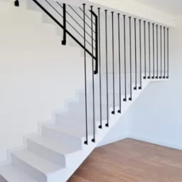 Białe schody z minimalistyczną czarną balustradą z pionowych prętów w nowoczesnym wnętrzu z drewnianą podłogą.