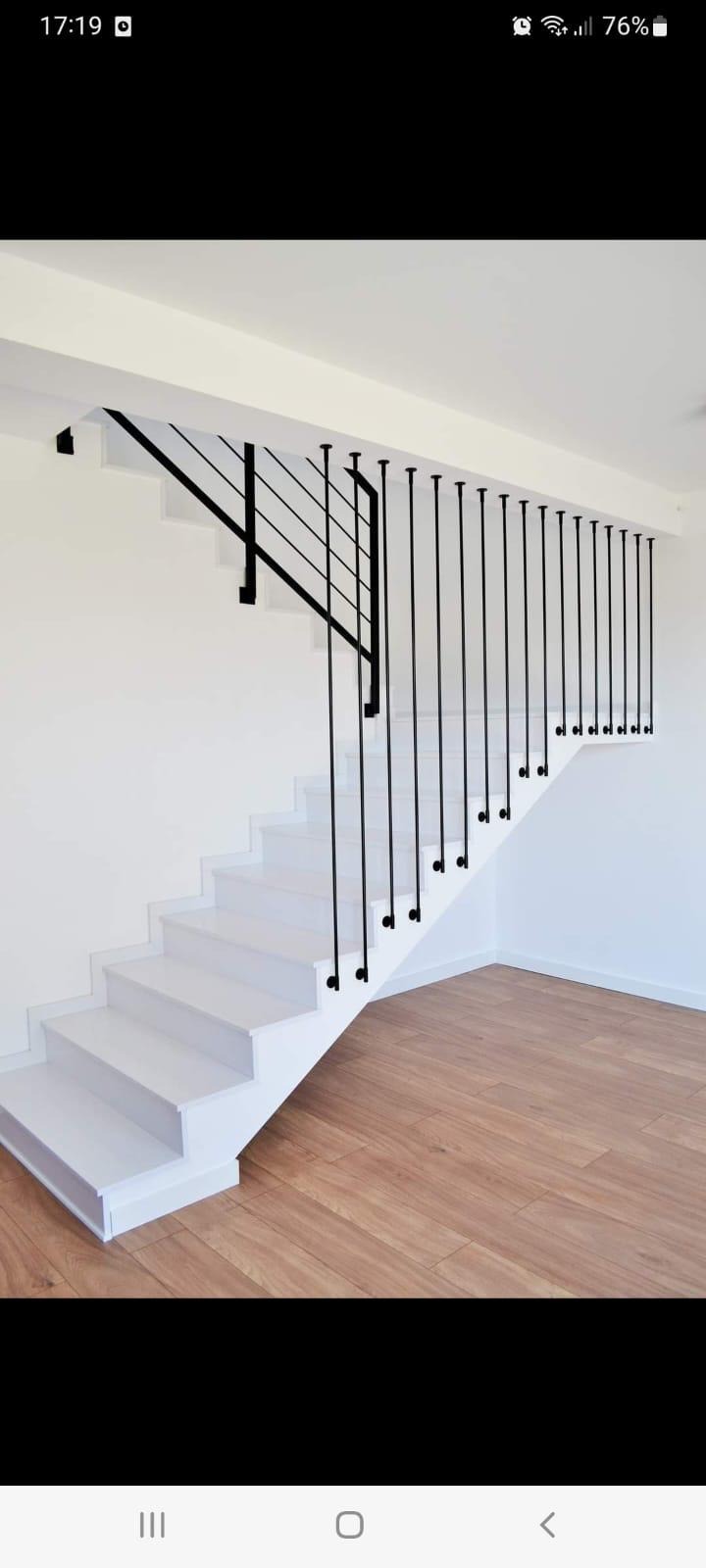 Białe schody z minimalistyczną czarną balustradą z pionowych prętów w nowoczesnym wnętrzu z drewnianą podłogą.