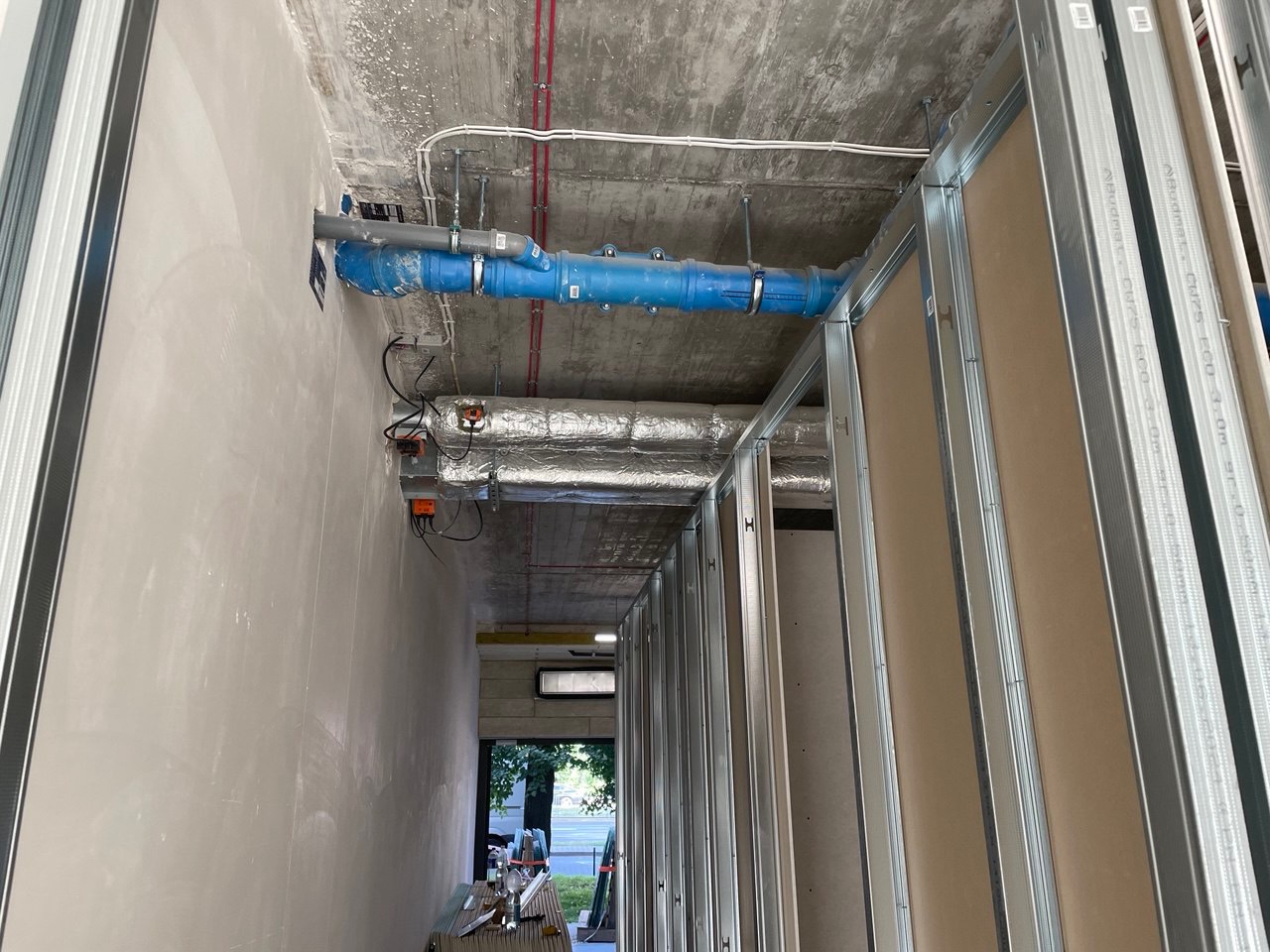 Wnętrze w trakcie remontu: widoczne szkielety ścian z płyt karton-gips, surowy betonowy sufit z instalacjami wentylacyjnymi i elektrycznymi, ściana po wstępnym szpachlowaniu, widok na zewnątrz...