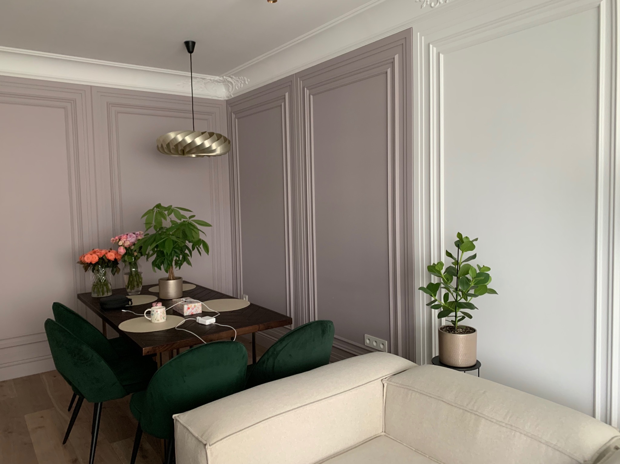 Eleganckie wnętrze: ściany wykończone panelami w odcieniach szarości i bieli, ciemny drewniany stół z zielonymi krzesłami, dekoracyjne kwiaty i rośliny, nowoczesna lampa wisząca.