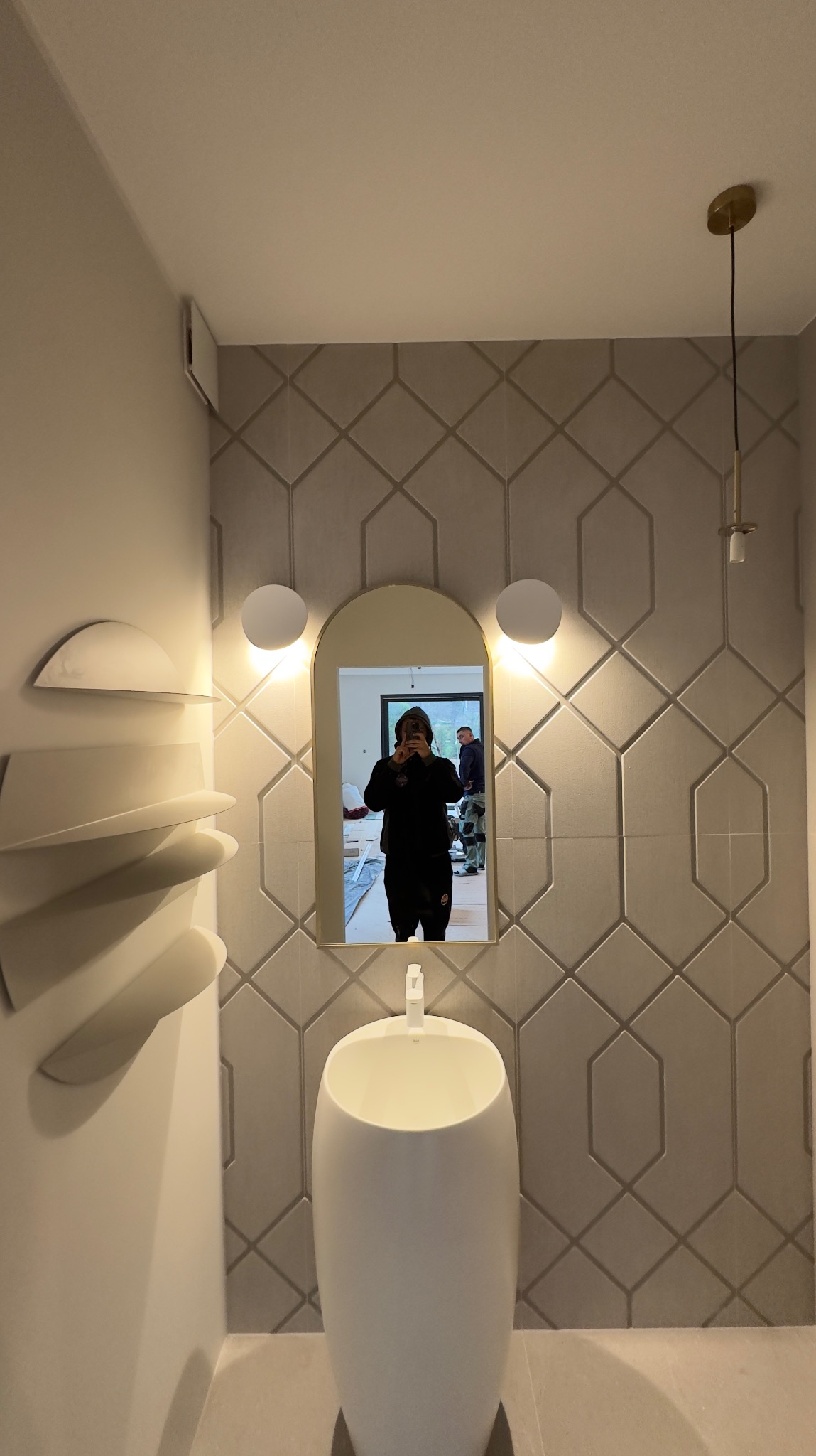 Nowoczesna łazienka z umywalką wolnostojącą, geometrycznymi płytkami na ścianie i podświetlanym lustrem, odbicie osoby robiącej zdjęcie w lustrze.