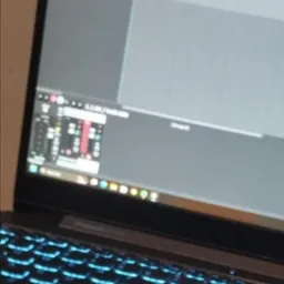 Laptop z podświetlaną klawiaturą i otwartym programem do obróbki audio na ekranie, widoczne miksery i puste ścieżki.