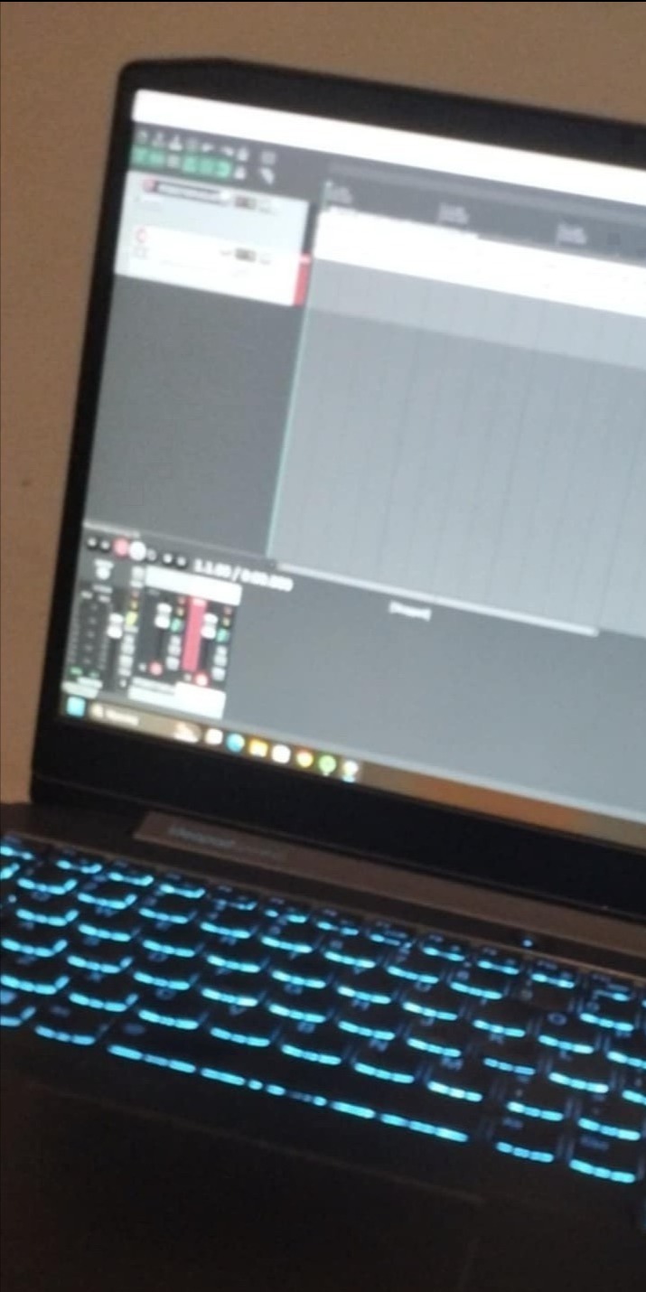 Laptop z podświetlaną klawiaturą i otwartym programem do obróbki audio na ekranie, widoczne miksery i puste ścieżki.