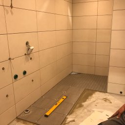 Piotr Kułagowski - Układanie płytek podłogowych w łazience w Piasku, widoczna poziomica na płytkach i przygotowane podejścia pod instalacje.