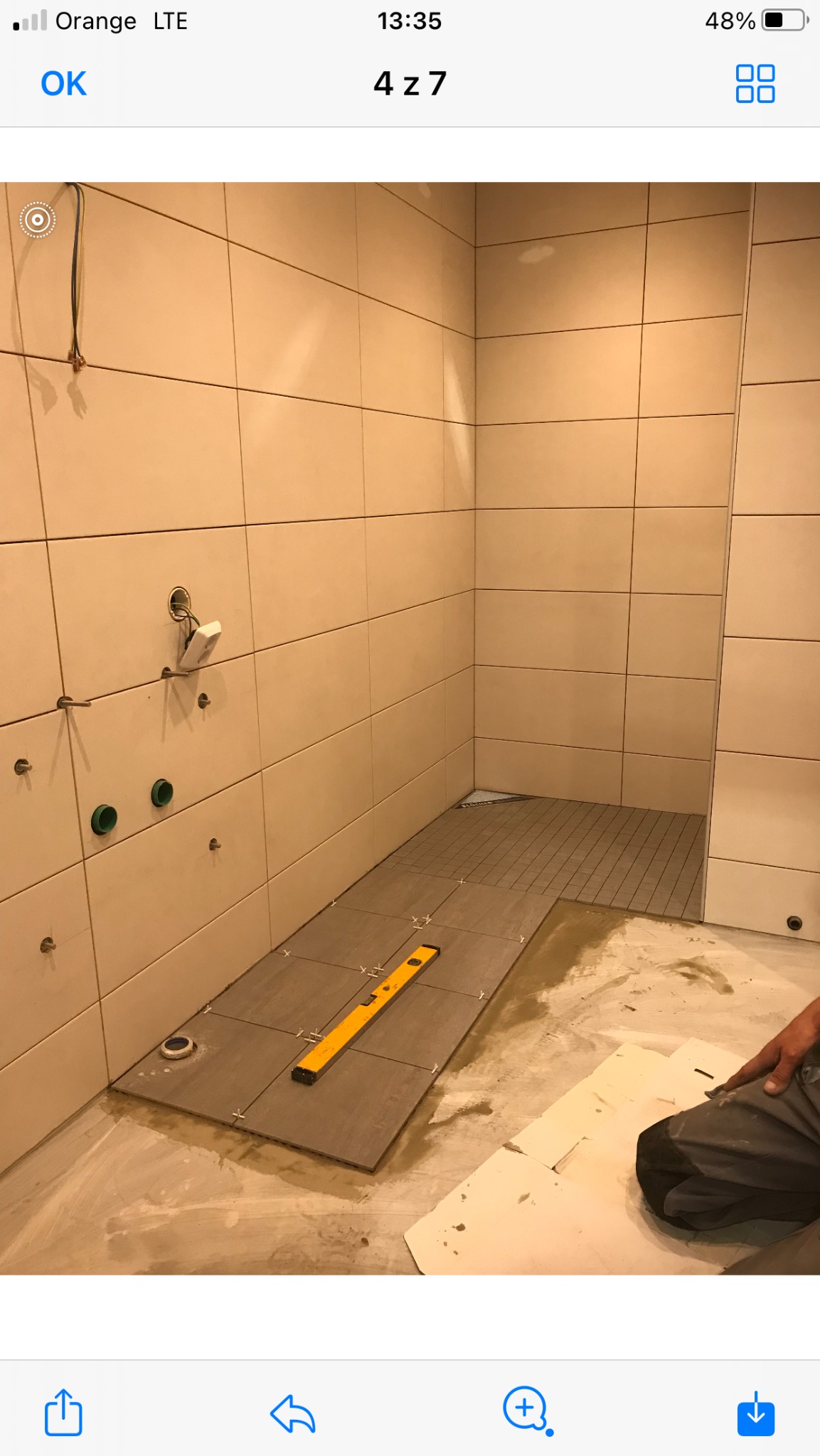 Układanie płytek podłogowych w łazience w Piasku, widoczna poziomica na płytkach i przygotowane podejścia pod instalacje.