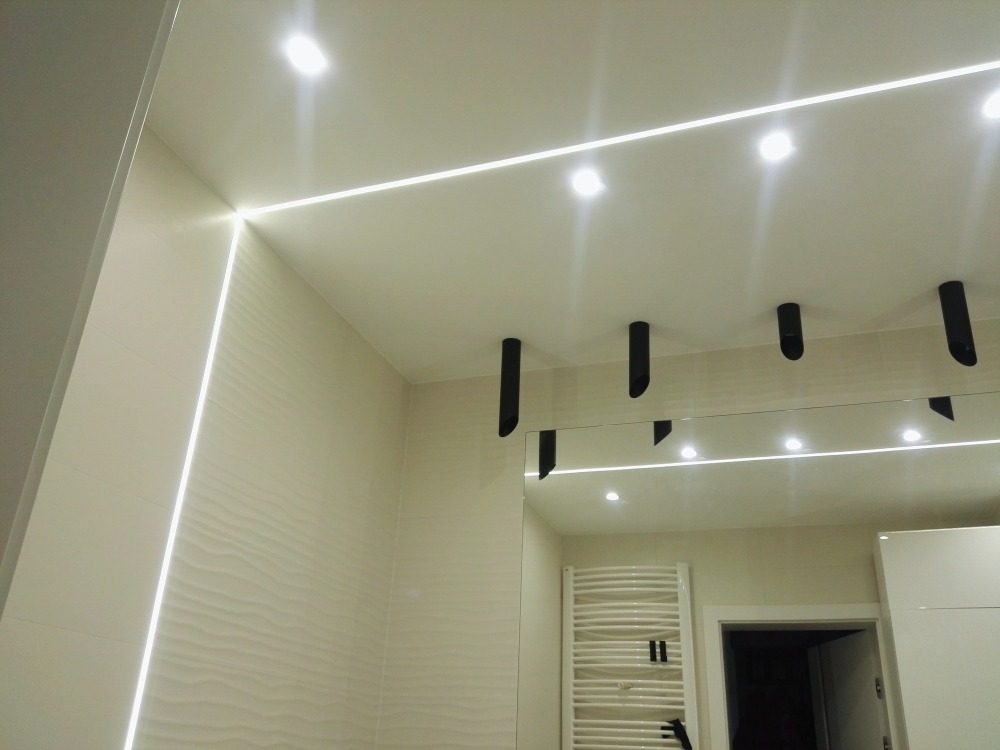 Nowoczesna łazienka z podświetlanym sufitem i ścianami, widoczne czarne elementy oświetleniowe i duże lustro.