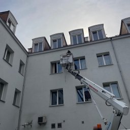 Tb went - Pracownik na podnośniku koszowym przy elewacji budynku z zamontowanymi klimatyzatorami, widoczne okna dachowe i klimatyzatory naścienne.