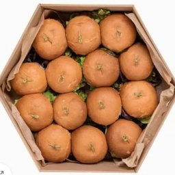 Pudelkowelove - Widok z góry na pudełko w kształcie sześciokąta wypełnione mini bułeczkami z dekoracyjnymi wykałaczkami, ułożonymi na zielonej sałacie.