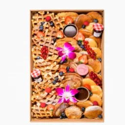 Eleganckie pudełko z goframi, naleśnikami, mini dżemami, sosem czekoladowym, posypane owocami i ozdobione kwiatami, idealne na prezent.