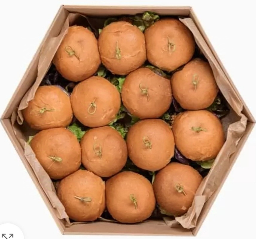 Widok z góry na pudełko w kształcie sześciokąta wypełnione mini bułeczkami z dekoracyjnymi wykałaczkami, ułożonymi na zielonej sałacie.