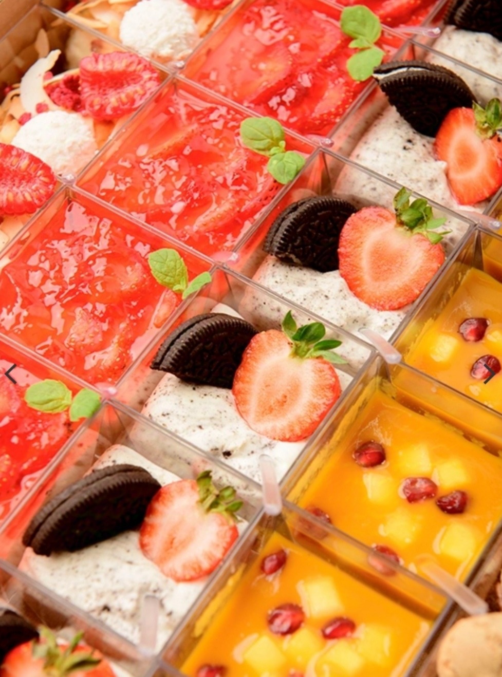 Różnorodne desery w przezroczystych pojemnikach: galaretka truskawkowa z miętą, krem z Oreo i truskawką, mango z granatem.