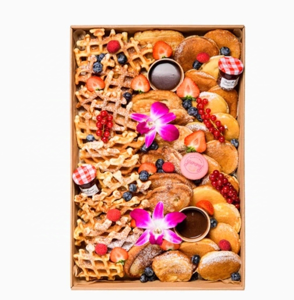 Eleganckie pudełko z goframi, naleśnikami, mini dżemami, sosem czekoladowym, posypane owocami i ozdobione kwiatami, idealne na prezent.