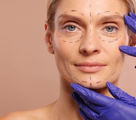 Twarz kobiety z zaznaczonymi liniami na skórze, przygotowywana do zabiegu, dłonie w fioletowych rękawiczkach dotykają twarzy.