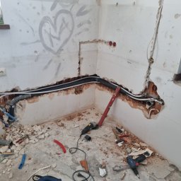 Ja siam - Ściana w trakcie prac instalacyjnych z widocznymi rurami, przewodami elektrycznymi, gruzem i narzędziami, na ścianie widnieje amatorski rysunek serca.